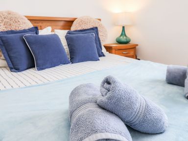 A bed with blue pillows and rolled towels with a bedside table and lamp at Navigators Rest in Whitby