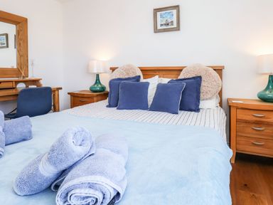 A bedroom with a wooden bed and blue pillows two bedside tables with lamps a dressing table with a mirror and a chair at Navigators Rest in Whitby