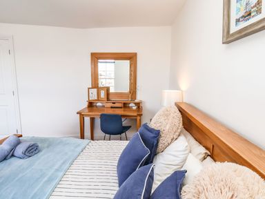 A bedroom with a bed with pillows and blankets a wooden desk with a mirror a lamp and a blue chair at Navigators Rest in Whitby
