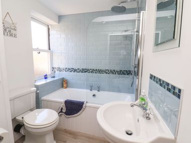 A bathroom with a toilet, bathtub with shower, sink, window, and light blue tiled walls at Navigators Rest in Whitby