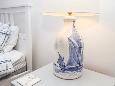 A bedside table with a lamp decorated with a blue sailboat design and part of a bed with blue and white bedding at Navigators Rest in Whitby