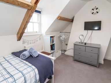 A bedroom with a single bed with folded towels dresser with TV and a standing fan under a sloped ceiling at Navigators Rest in Whitby