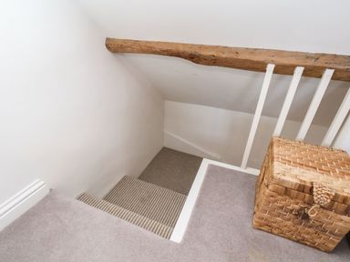 A stairway with striped carpet and white walls next to a woven wicker basket at Navigators Rest in Whitby