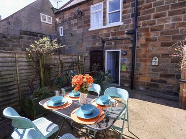 An outdoor patio with a metal table and blue chairs set for four with plates bowls and glasses at Navigators Rest in Whitby
