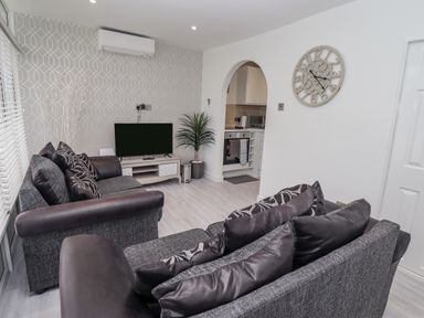 A living room with two sofas cushions television plant and wall clock at 19 Cherry Park in Chapel St Leonards