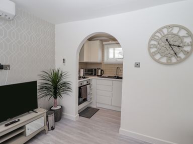 A living room with a television and plant next to an arched doorway leading to a kitchen with white cabinets at 19 Cherry Park in Chapel St Leonards