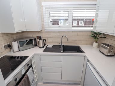 A kitchen countertop with a microwave kettle sink toaster and potted plant at 19 Cherry Park in Chapel St Leonards