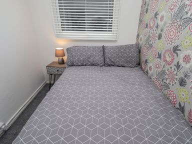 A bedroom with a bed with geometric patterned bedding a nightstand with a lamp and floral wallpaper at 19 Cherry Park in Chapel St Leonards
