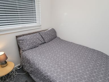 A bedroom with a double bed with patterned bedding a side table with a lamp and a window at 19 Cherry Park in Chapel St Leonards