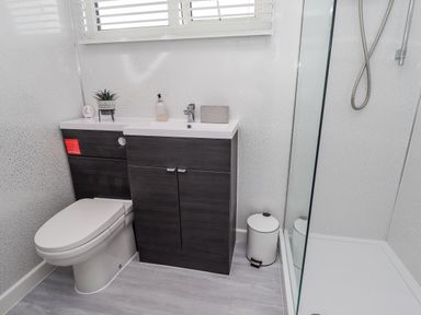 A bathroom with a toilet sink cabinet shower and a small waste bin at 19 Cherry Park in Chapel St Leonards