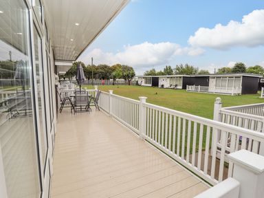 A deck with outdoor furniture and umbrella overlooking grass and black and white buildings at 19 Cherry Park in Chapel St Leonards