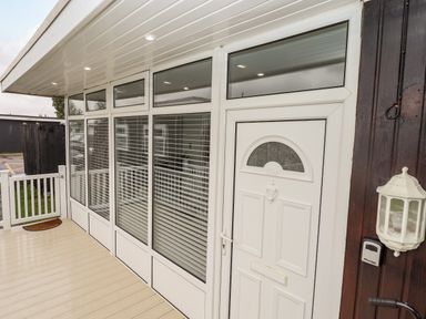 A white front door with windows and blinds on a porch with a light and doorbell at 19 Cherry Park in Chapel St Leonards
