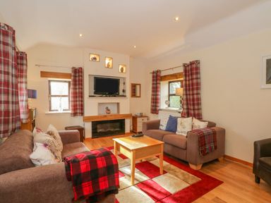 A living room with two sofas a wooden coffee table and a wall-mounted television at Burnt Oak Stables in Mynydd Isa