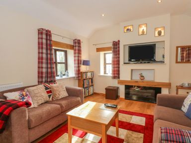 A living room with two brown sofas a wooden coffee table a wall-mounted TV and red plaid curtains at Burnt Oak Stables in Mynydd Isa