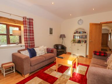 A living room with two sofas a coffee table a bookshelf and a window with red plaid curtains at Burnt Oak Stables in Mynydd Isa