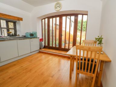 A kitchen with wooden floor a wooden table with two chairs a turquoise microwave and glass doors leading outside at Burnt Oak Stables in Mynydd Isa