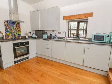 A kitchen with grey cabinets a colorful backsplash oven microwave and a window with wooden blinds at Burnt Oak Stables in Mynydd Isa