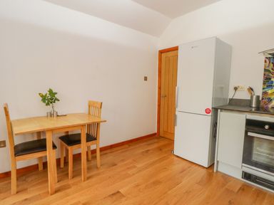 A kitchen with a wooden dining table and two chairs a white fridge a wooden door and a built-in oven at Burnt Oak Stables in Mynydd Isa