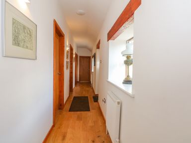 A hallway with wooden floors doors and beams with a window ledge holding a decorative lamp at Burnt Oak Stables in Mynydd Isa