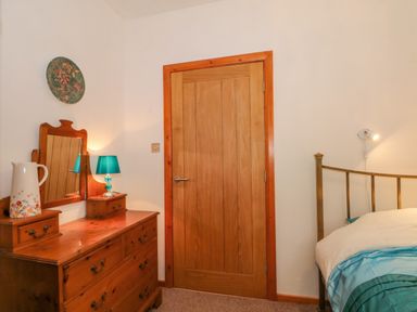 A bedroom corner with a wooden dresser mirror lamp and door next to a bed with a metal frame at Burnt Oak Stables in Mynydd Isa
