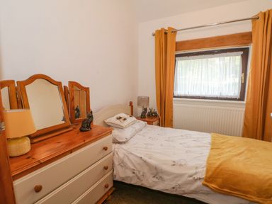 A bedroom with a single bed next to a window and a dresser with a mirror and lamp at Burnt Oak Stables in Mynydd Isa