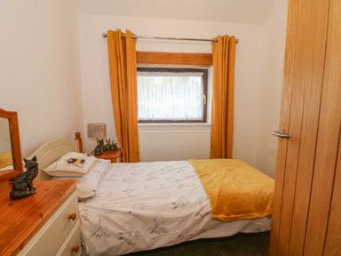 A small bedroom with a bed near a window with orange curtains and a dresser with animal figurines at Burnt Oak Stables in Mynydd Isa