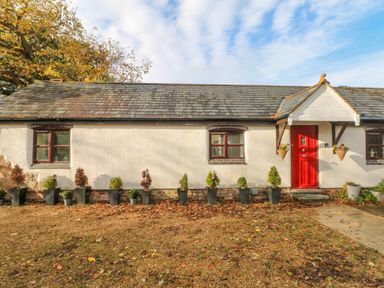A single story building with a red door two windows and potted plants outside at Burnt Oak Stables in Mynydd Isa