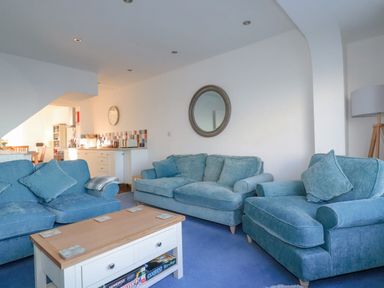 A living room with blue sofas a wooden coffee table and a round mirror on the wall at Sea View in Mevagissey