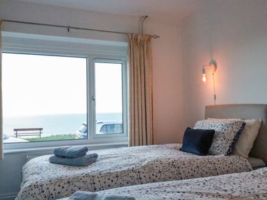 A bedroom with two single beds facing a window with a sea view at Sea View in Mevagissey