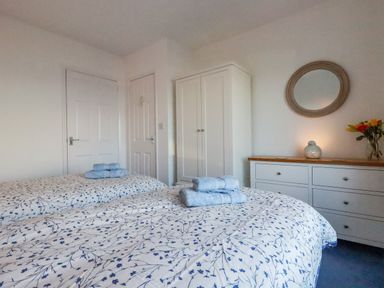 A bedroom with two beds with floral bedding and towels a white wardrobe a white dresser with a mirror and flowers at Sea View in Mevagissey
