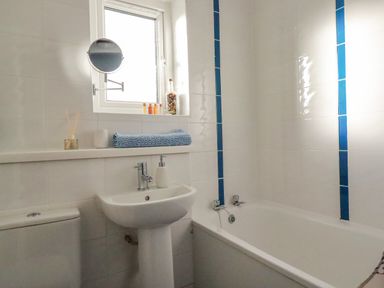 A bathroom with a bathtub sink toilet window and a blue towel on a shelf at Sea View in Mevagissey