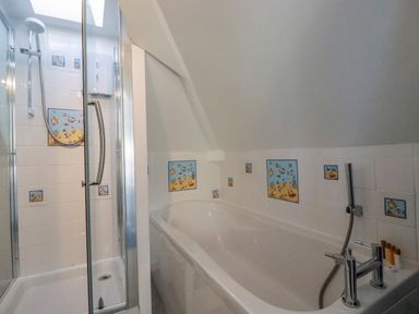 A bathroom with a shower enclosure and a bathtub with marine-themed tiles at Sea View in Mevagissey