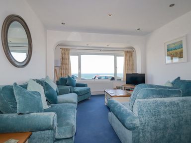 A living room with blue sofas a coffee table a TV and a window with a sea view at Sea View in Mevagissey