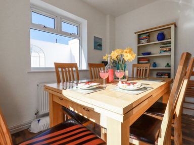 A dining area with a wooden table set with plates of food glasses and flowers near a window and bookshelf at Sea View in Mevagissey