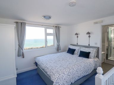 A bedroom with a double bed beside a window overlooking the sea at Sea View Mevagissey