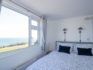 A bedroom with a bed and bedside lamps next to a window showing a sea view at Sea View in Mevagissey