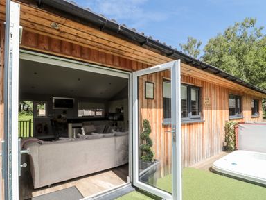 An open door leads from a wooden cabin to a living room with a sofa and kitchen inside at Lodge 32 Otterburn