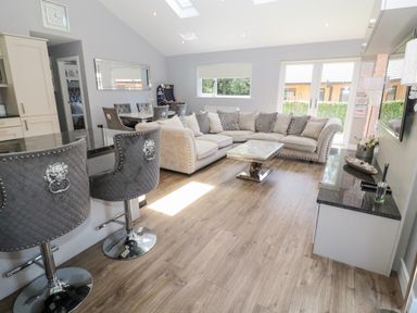 A living room with an L shaped sofa a marble coffee table bar stools and a dining area at Lodge 32 in Otterburn
