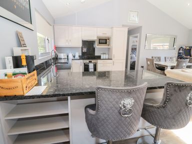 A modern kitchen with a black granite countertop island and two gray upholstered chairs with lion handles at Lodge 32 in Otterburn