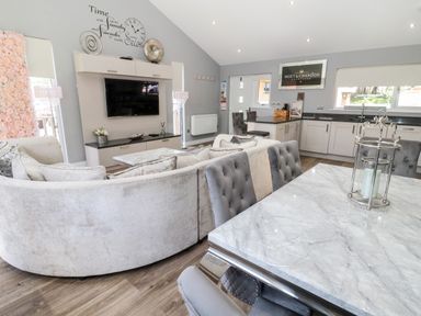 An open plan living room and kitchen with a circular sofa a wall mounted TV and a marble dining table at Lodge 32 Otterburn