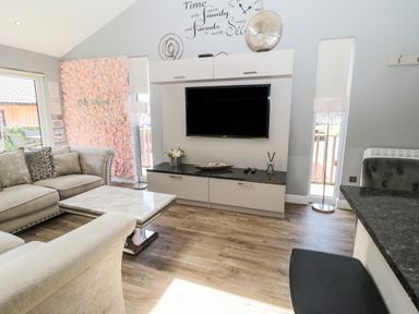 A living room with a wall-mounted TV a flower wall sofa and a marble coffee table at Lodge 32 in Otterburn