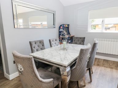 A dining area with a marble table, six grey tufted chairs, a wall mirror, a window, and a Space Invaders arcade machine at Lodge 32 in Otterburn