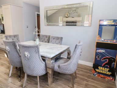 A dining area with a rectangular marble table and six gray upholstered chairs with silver handles and a decorative mirror on the wall at Lodge 32 in Otterburn