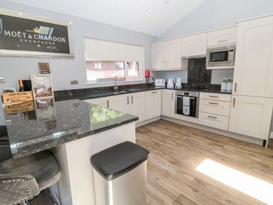 A kitchen with white cabinets black countertops a stove microwave toaster and bar stools at Lodge 32 in Otterburn
