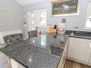A kitchen with a granite countertop two cushioned chairs a door a radiator and a Moet and Chandon sign at Lodge 32 in Otterburn