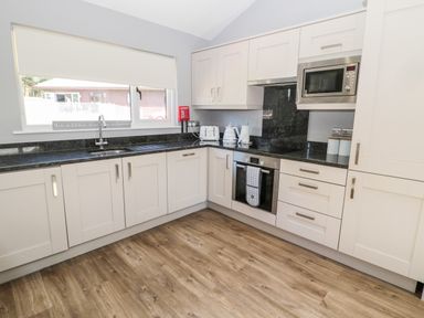 A kitchen with white cabinets black countertops a window and wooden floor at Lodge 32 in Otterburn