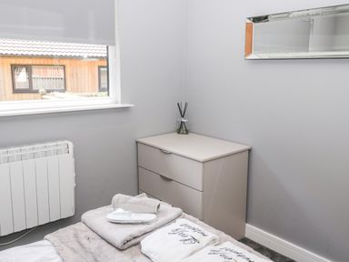 A bedroom corner with a chest of drawers and window showing a wooden building outside at Lodge 32 in Otterburn