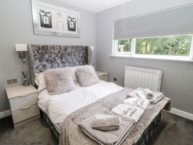 A bedroom with a bed featuring a tufted headboard two nightstands and a window with a roller blind at Lodge 32 Otterburn