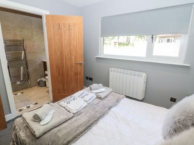 A bedroom with a bed and towels on it next to a window and an open door leading to a bathroom at Lodge 32 in Otterburn