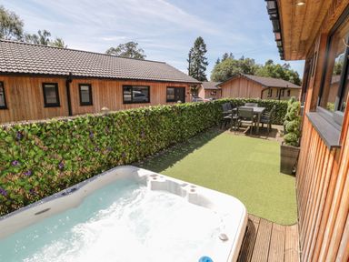 An outdoor patio area with a hot tub a dining table with chairs and wooden buildings at Lodge 32 in Otterburn